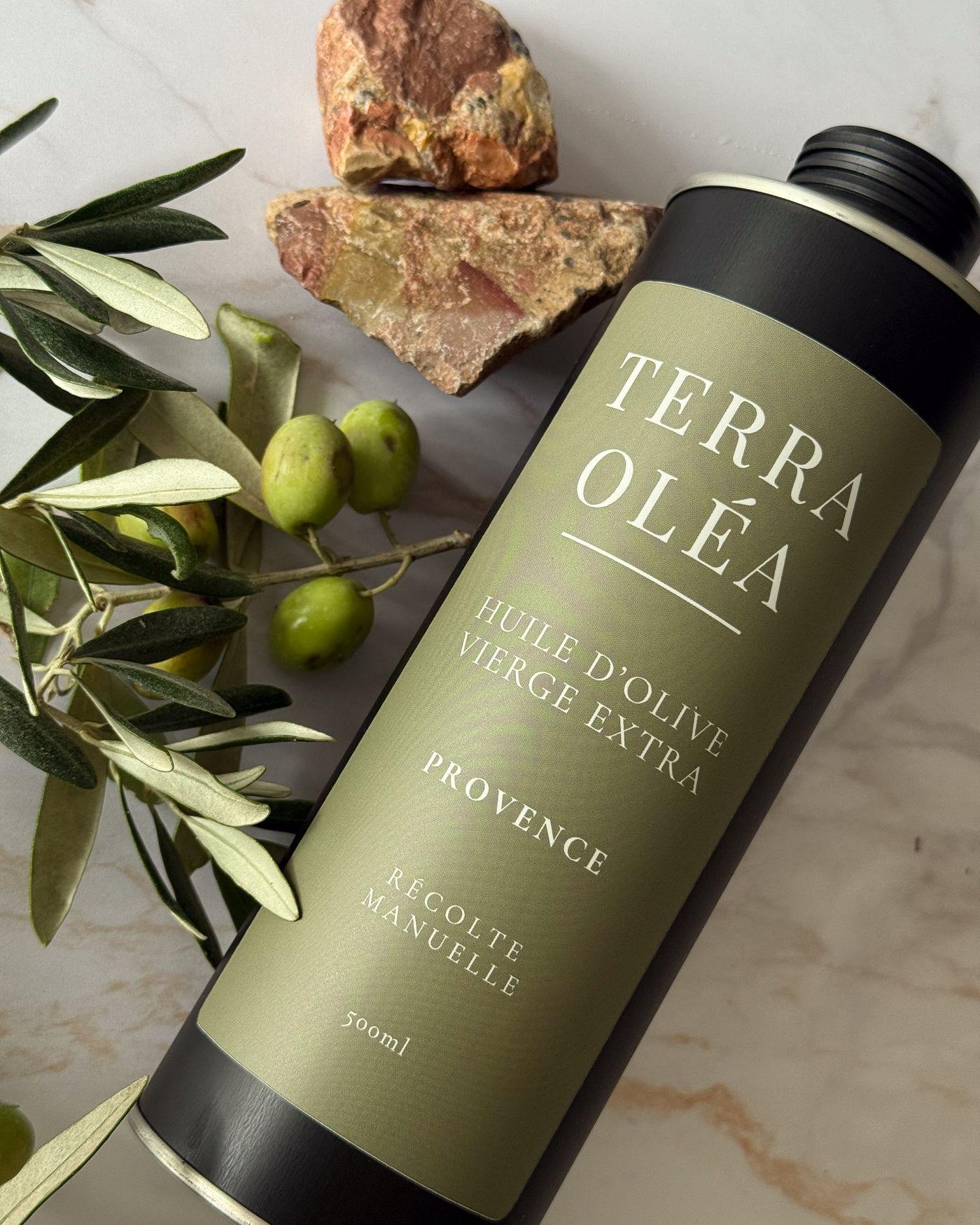 Bidon Terra Oléa posé sur du marbre, avec des branches d'olivier et des olives vertes