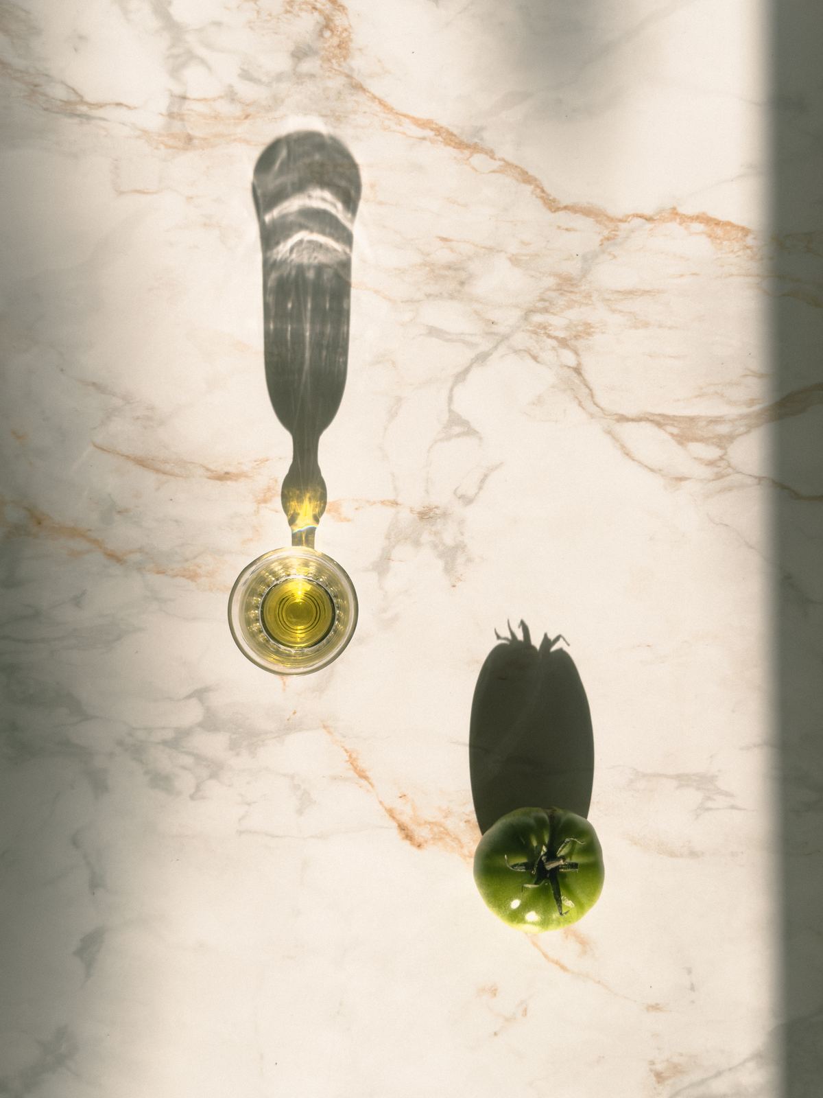 Verre d'huile d'olive vierge extra Terra Oléa en plein soleil sur du marbre, tomate verte
